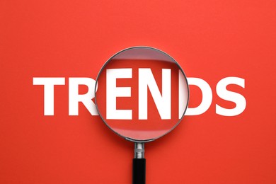 Image of Word Trends and magnifying glass on red background, top view