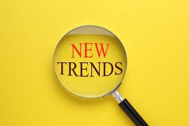 Image of New trends. Magnifying glass on yellow background, top view