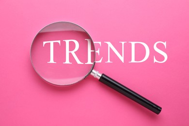 Image of Word Trends and magnifying glass on pink background, top view