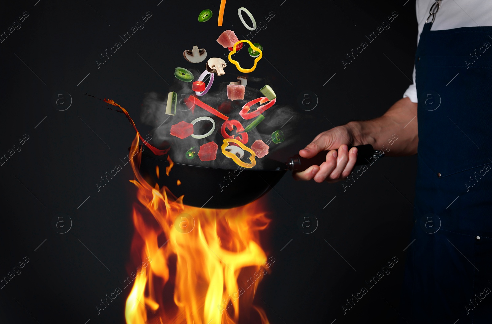 Professional chef tossing vegetables and meat pieces in wok on black background, closeup Image of Professional chef tossing vegetables and meat pieces in wok on black background, closeup
