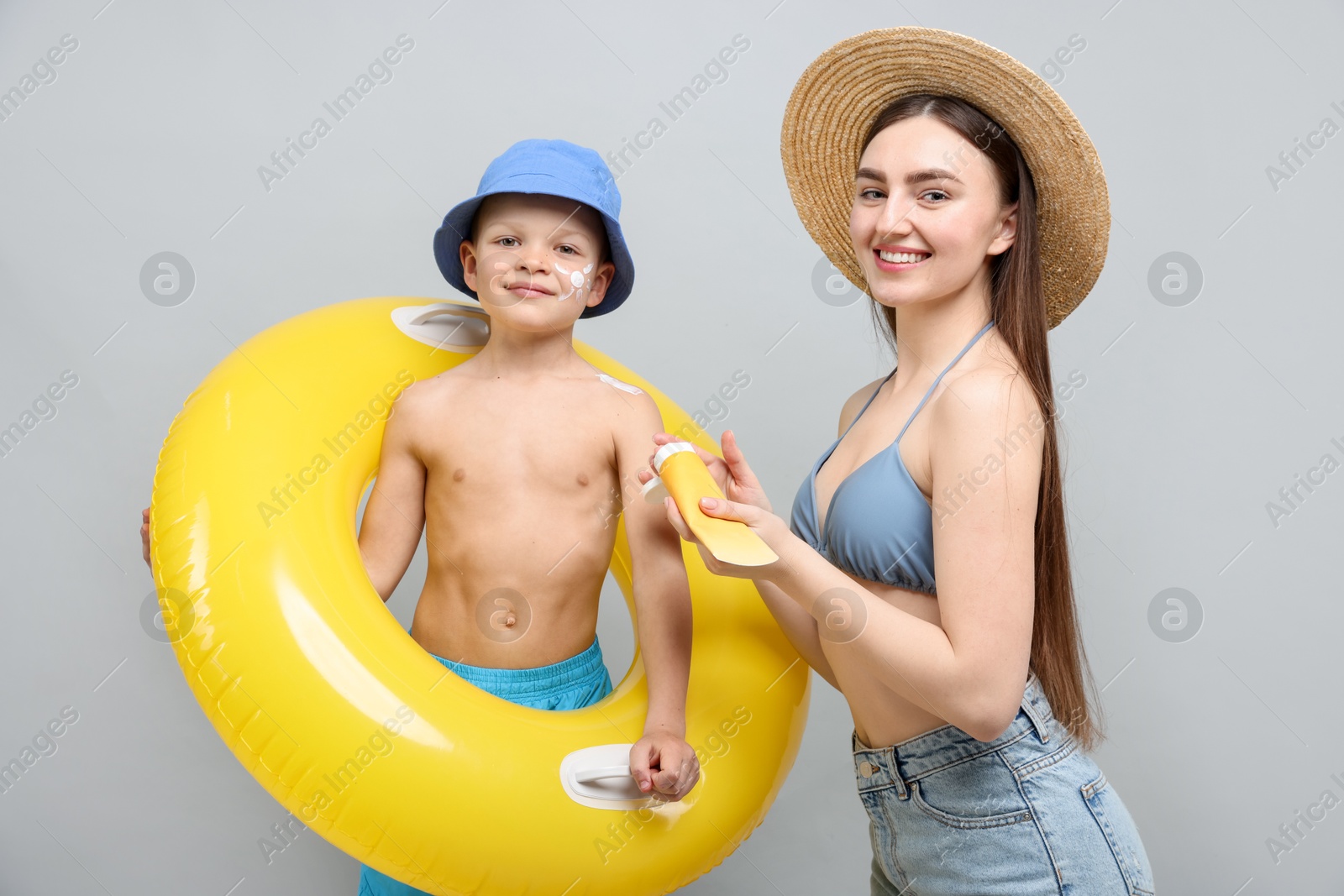 Mother with sun protection cream and her son on light grey background Photo of Mother with sun protection cream and her son on light grey background