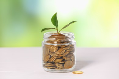 Photo of Investment concept. Glass jar with coins and sprout on light table against blurred green background