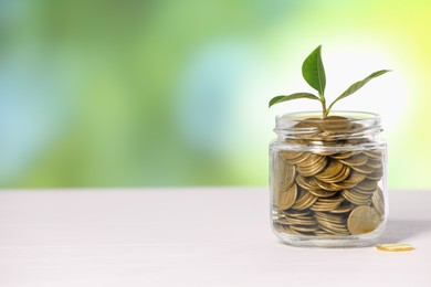 Photo of Investment concept. Glass jar with coins and sprout on light table against blurred green background, space for text