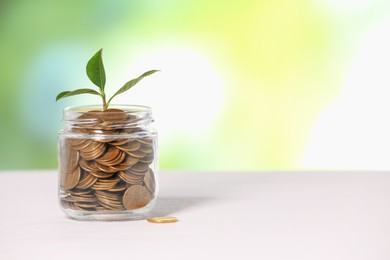 Photo of Investment concept. Glass jar with coins and sprout on light table against blurred green background, space for text