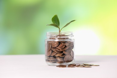 Photo of Investment concept. Glass jar with coins and sprout on light table against blurred green background