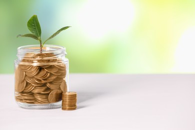 Photo of Investment concept. Glass jar with coins and sprout on light table against blurred green background, space for text