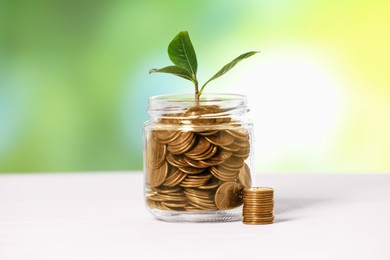 Photo of Investment concept. Glass jar with coins and sprout on light table against blurred green background