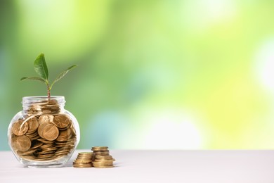 Photo of Investment concept. Glass jar with coins and sprout on light table against blurred green background, space for text