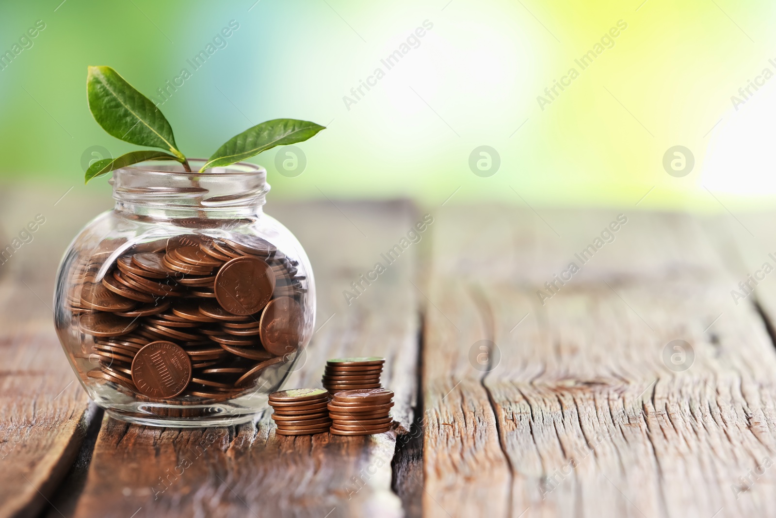 Investment concept. Glass jar with coins and sprout on wooden table against blurred green background, space for text Photo of Investment concept. Glass jar with coins and sprout on wooden table against blurred green background, space for text