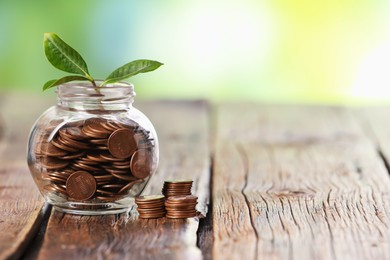 Photo of Investment concept. Glass jar with coins and sprout on wooden table against blurred green background, space for text