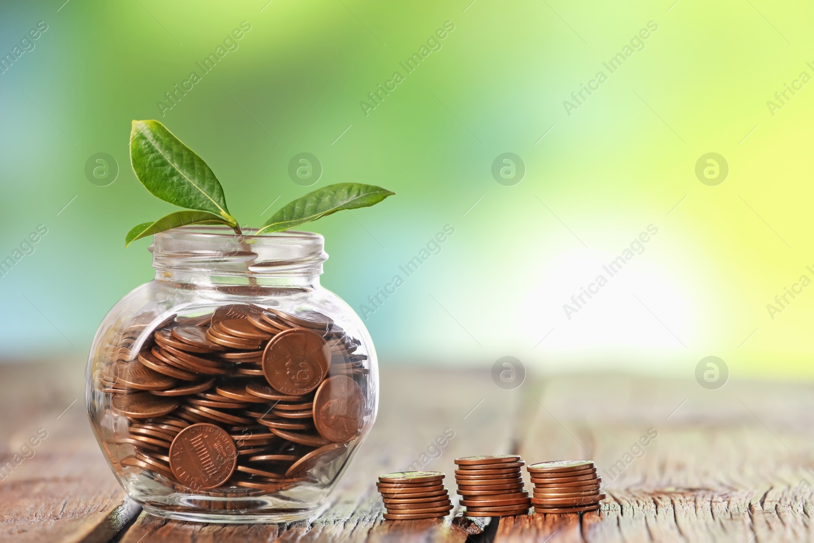 Investment concept. Glass jar with coins and sprout on wooden table against blurred green background, space for text Photo of Investment concept. Glass jar with coins and sprout on wooden table against blurred green background, space for text