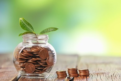 Photo of Investment concept. Glass jar with coins and sprout on wooden table against blurred green background, space for text