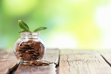 Photo of Investment concept. Glass jar with coins and sprout on wooden table against blurred green background, space for text