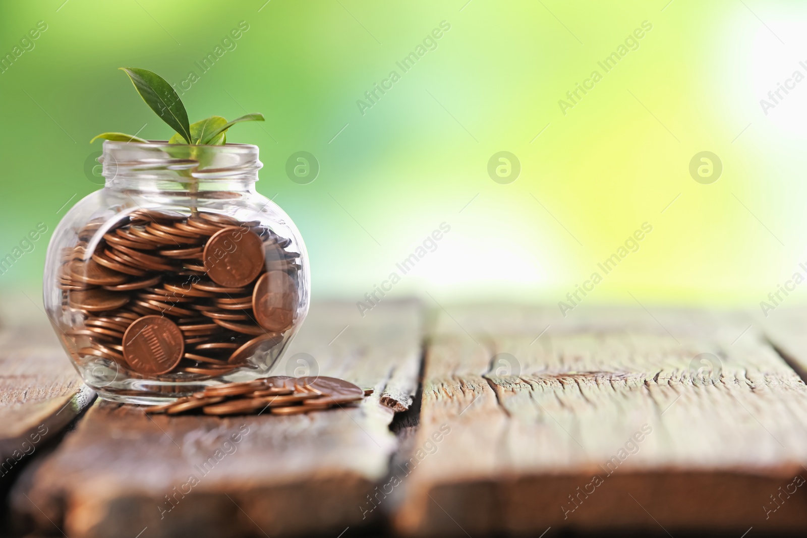 Investment concept. Glass jar with coins and sprout on wooden table against blurred green background, space for text Photo of Investment concept. Glass jar with coins and sprout on wooden table against blurred green background, space for text