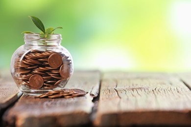Photo of Investment concept. Glass jar with coins and sprout on wooden table against blurred green background, space for text