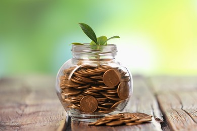 Photo of Investment concept. Glass jar with coins and sprout on wooden table against blurred green background