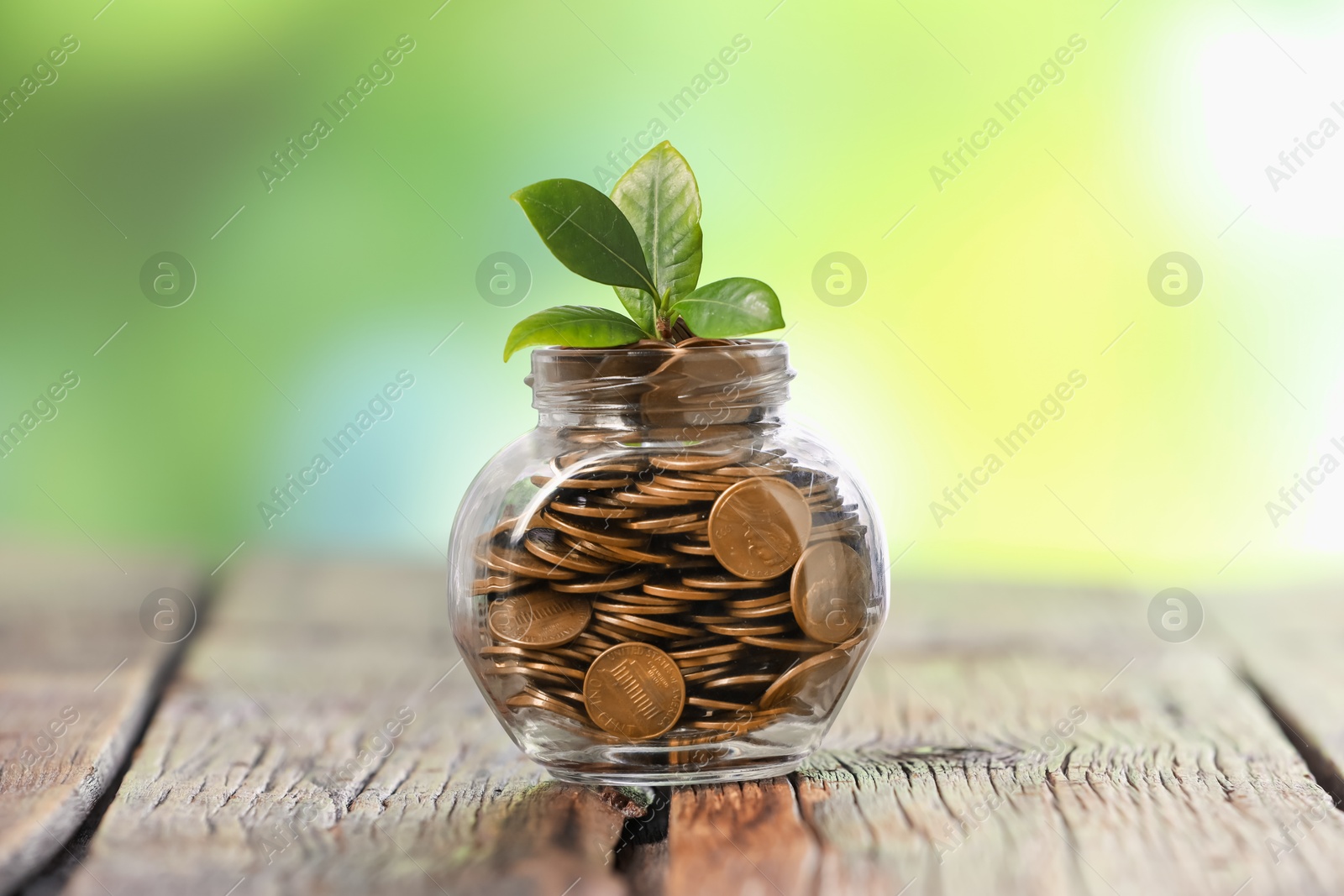 Investment concept. Glass jar with coins and sprout on wooden table against blurred green background Photo of Investment concept. Glass jar with coins and sprout on wooden table against blurred green background