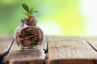 Photo of Investment concept. Glass jar with coins and sprout on wooden table against blurred green background, space for text