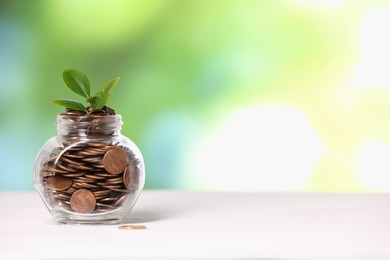 Photo of Investment concept. Glass jar with coins and sprout on light table against blurred green background, space for text