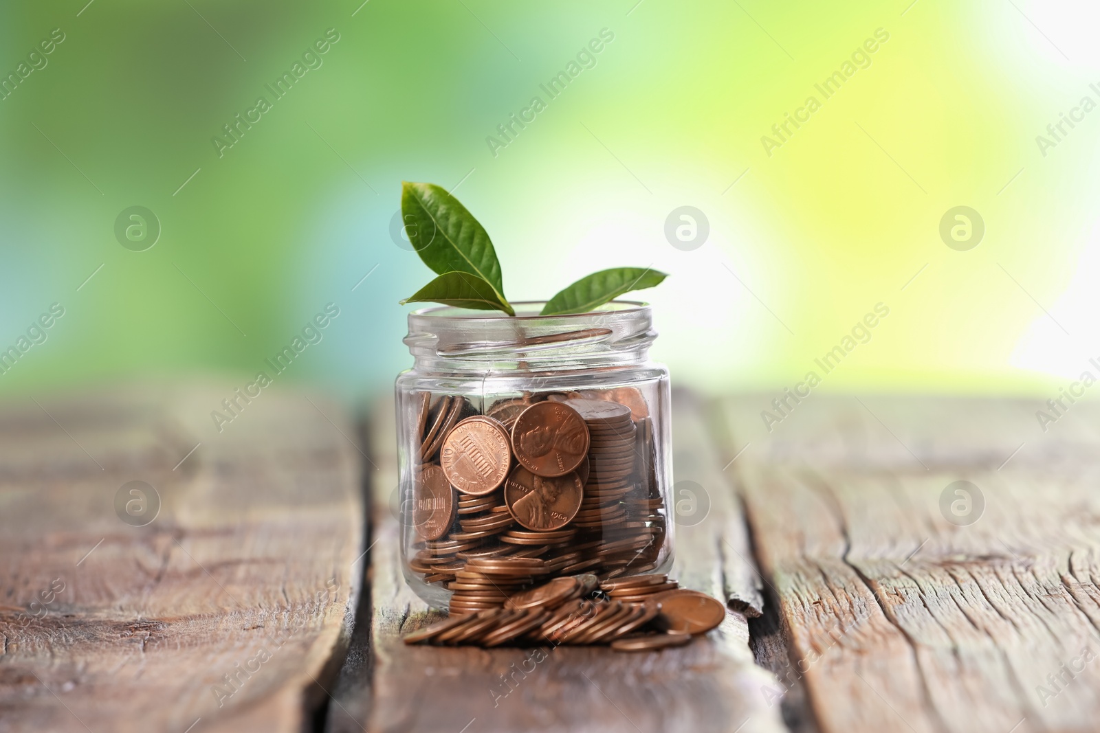 Investment concept. Glass jar with coins and sprout on wooden table against blurred green background Photo of Investment concept. Glass jar with coins and sprout on wooden table against blurred green background