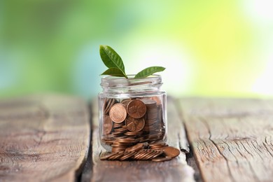 Photo of Investment concept. Glass jar with coins and sprout on wooden table against blurred green background