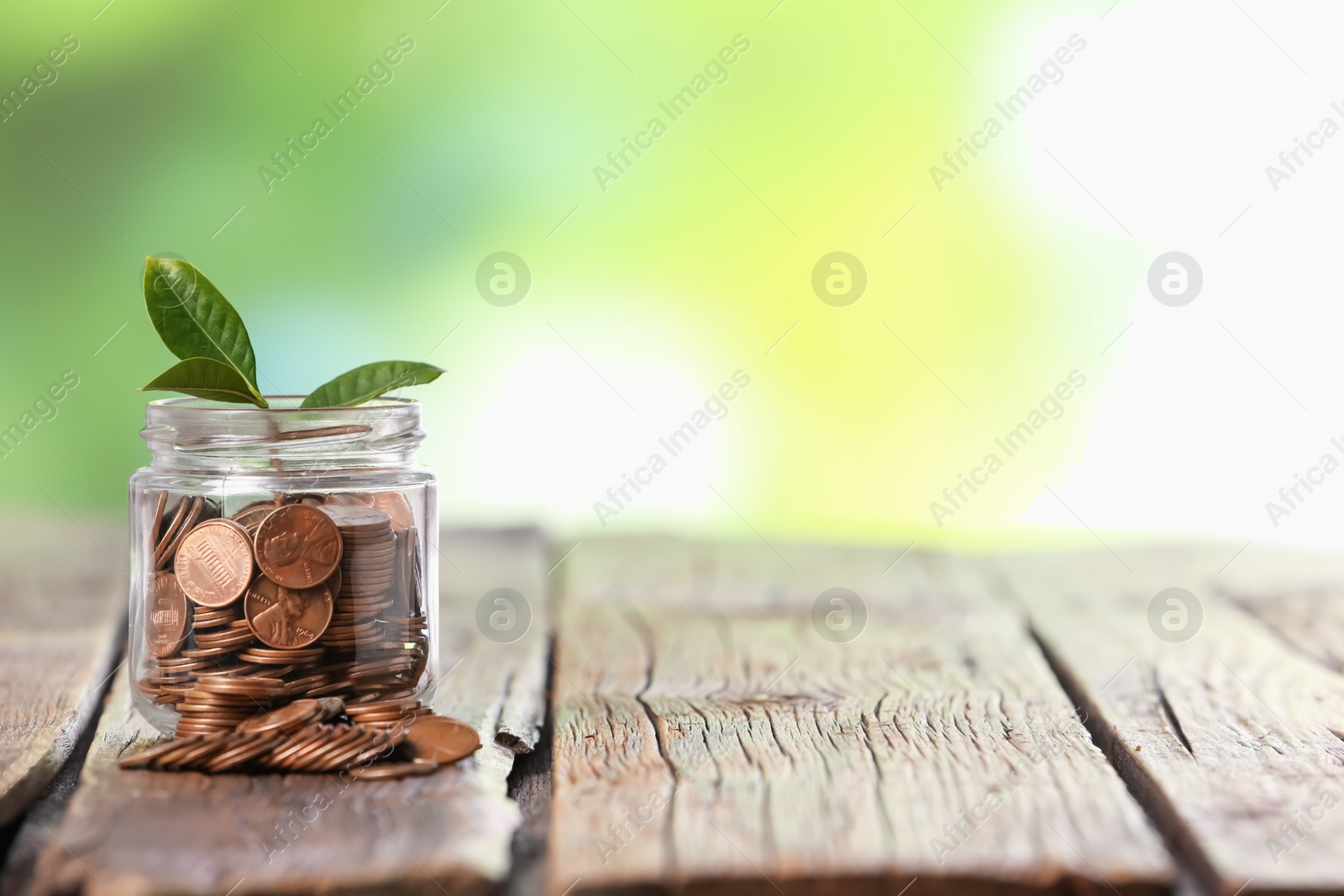 Investment concept. Glass jar with coins and sprout on wooden table against blurred green background, space for text Photo of Investment concept. Glass jar with coins and sprout on wooden table against blurred green background, space for text