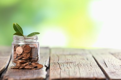Photo of Investment concept. Glass jar with coins and sprout on wooden table against blurred green background, space for text