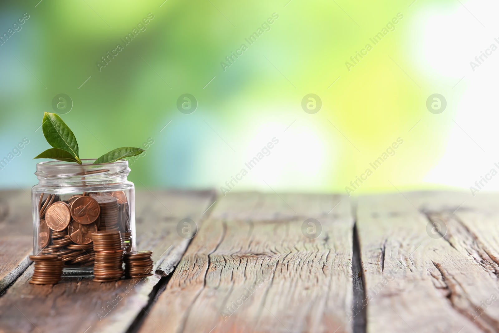 Investment concept. Glass jar with coins and sprout on wooden table against blurred green background, space for text Photo of Investment concept. Glass jar with coins and sprout on wooden table against blurred green background, space for text