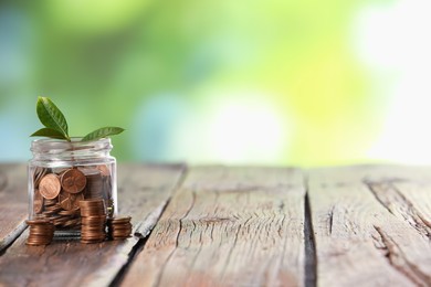 Photo of Investment concept. Glass jar with coins and sprout on wooden table against blurred green background, space for text