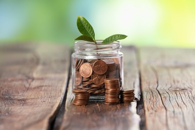Photo of Investment concept. Glass jar with coins and sprout on wooden table against blurred green background