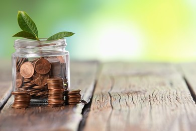 Photo of Investment concept. Glass jar with coins and sprout on wooden table against blurred green background, space for text