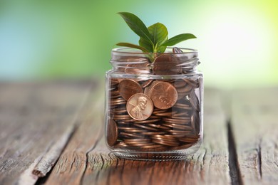 Photo of Investment concept. Glass jar with coins and sprout on wooden table against blurred green background