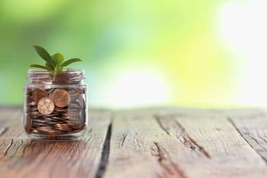 Photo of Investment concept. Glass jar with coins and sprout on wooden table against blurred green background, space for text