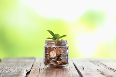 Photo of Investment concept. Glass jar with coins and sprout on wooden table against blurred green background