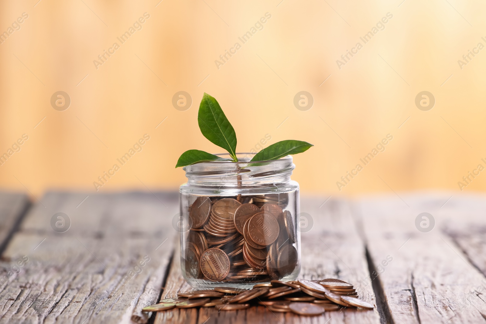 Investment concept. Glass jar with coins and sprout on wooden table against blurred orange background Photo of Investment concept. Glass jar with coins and sprout on wooden table against blurred orange background