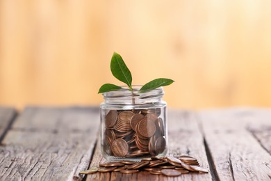 Photo of Investment concept. Glass jar with coins and sprout on wooden table against blurred orange background