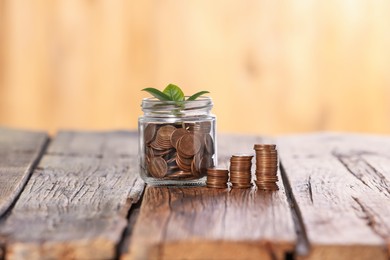 Photo of Investment concept. Glass jar with coins and sprout on wooden table against blurred orange background