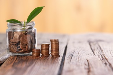 Photo of Investment concept. Glass jar with coins and sprout on wooden table against blurred orange background, space for text