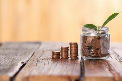 Photo of Investment concept. Glass jar with coins and sprout on wooden table against blurred orange background, space for text