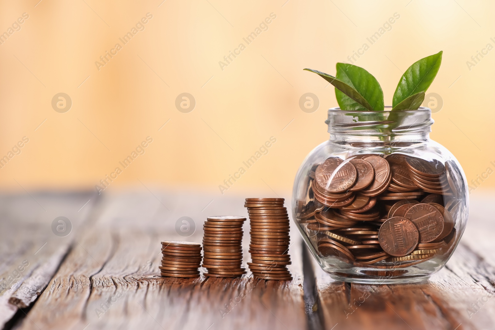 Investment concept. Glass jar with coins and sprout on wooden table against blurred orange background Photo of Investment concept. Glass jar with coins and sprout on wooden table against blurred orange background