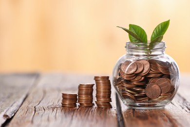 Photo of Investment concept. Glass jar with coins and sprout on wooden table against blurred orange background