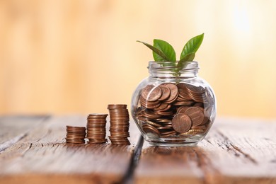 Photo of Investment concept. Glass jar with coins and sprout on wooden table against blurred orange background