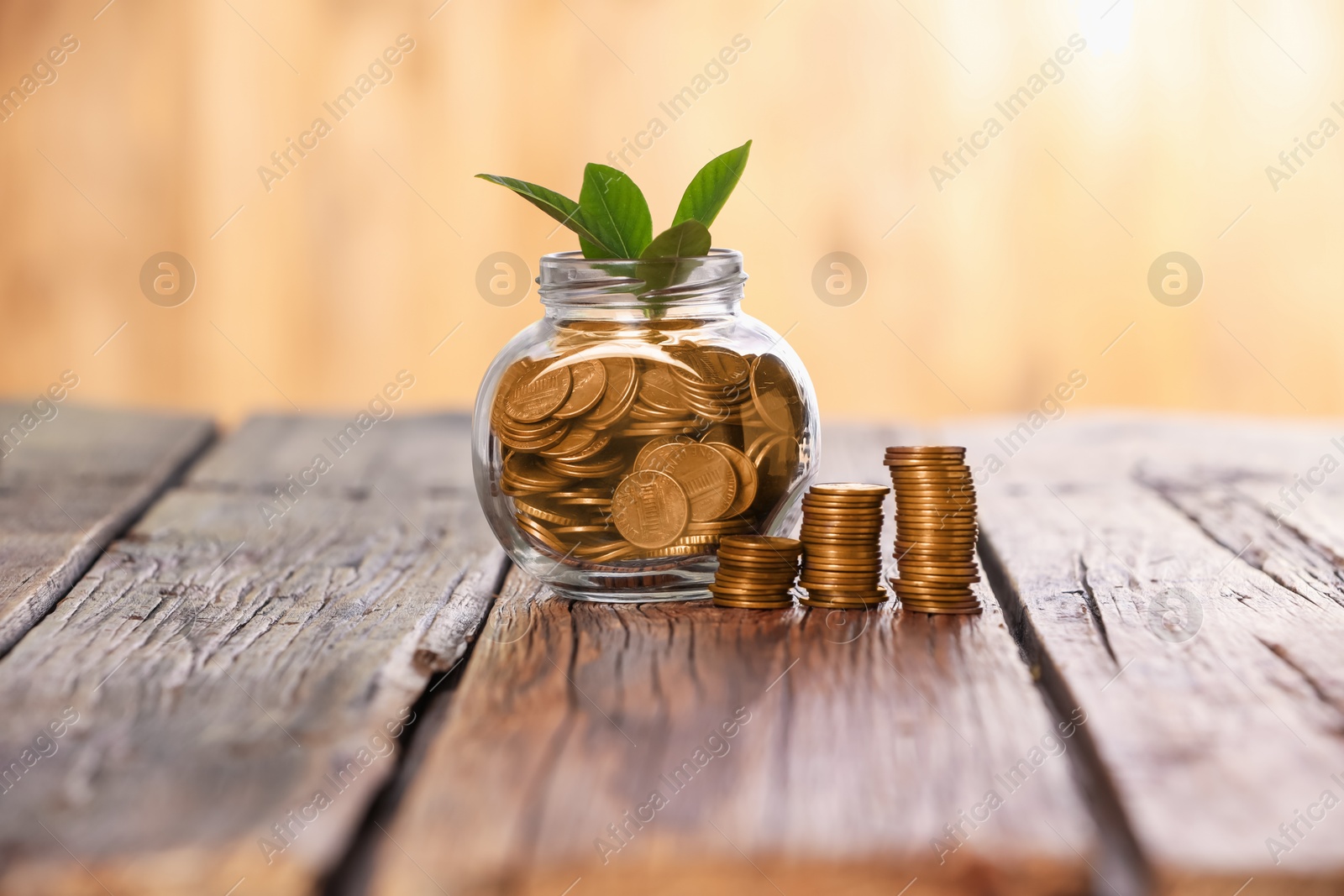 Investment concept. Glass jar with coins and sprout on wooden table against blurred orange background Photo of Investment concept. Glass jar with coins and sprout on wooden table against blurred orange background