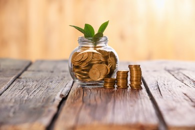Photo of Investment concept. Glass jar with coins and sprout on wooden table against blurred orange background