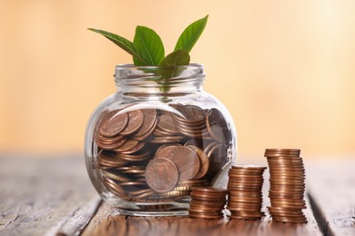Photo of Investment concept. Glass jar with coins and sprout on wooden table against blurred orange background