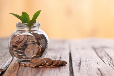 Photo of Investment concept. Glass jar with coins and sprout on wooden table against blurred orange background, space for text