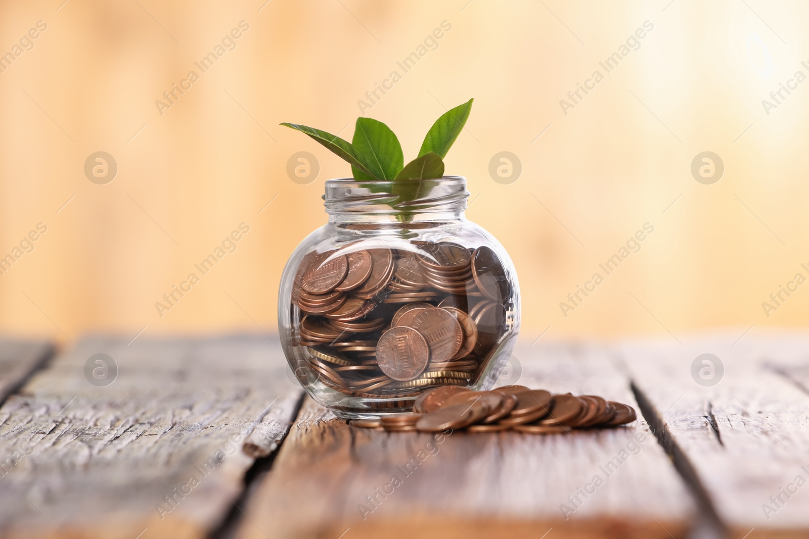 Investment concept. Glass jar with coins and sprout on wooden table against blurred orange background Photo of Investment concept. Glass jar with coins and sprout on wooden table against blurred orange background