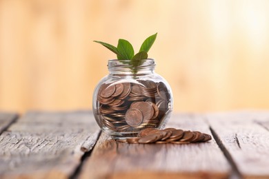 Photo of Investment concept. Glass jar with coins and sprout on wooden table against blurred orange background