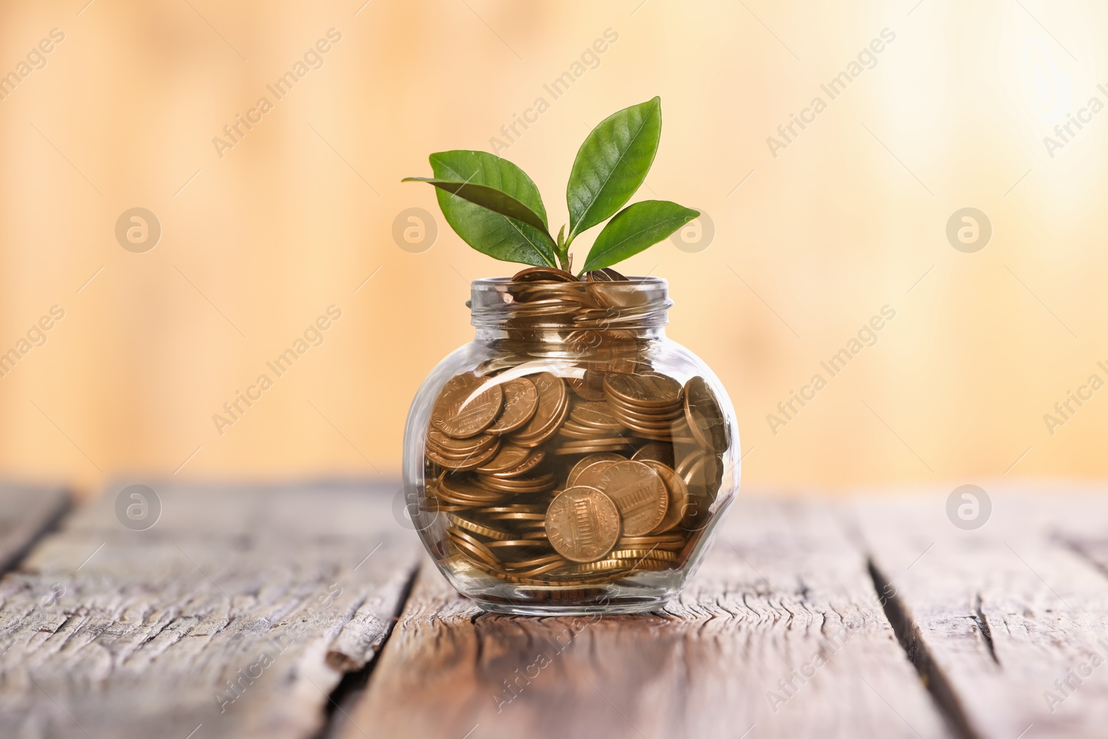 Investment concept. Glass jar with coins and sprout on wooden table against blurred orange background Photo of Investment concept. Glass jar with coins and sprout on wooden table against blurred orange background
