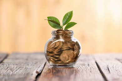 Photo of Investment concept. Glass jar with coins and sprout on wooden table against blurred orange background